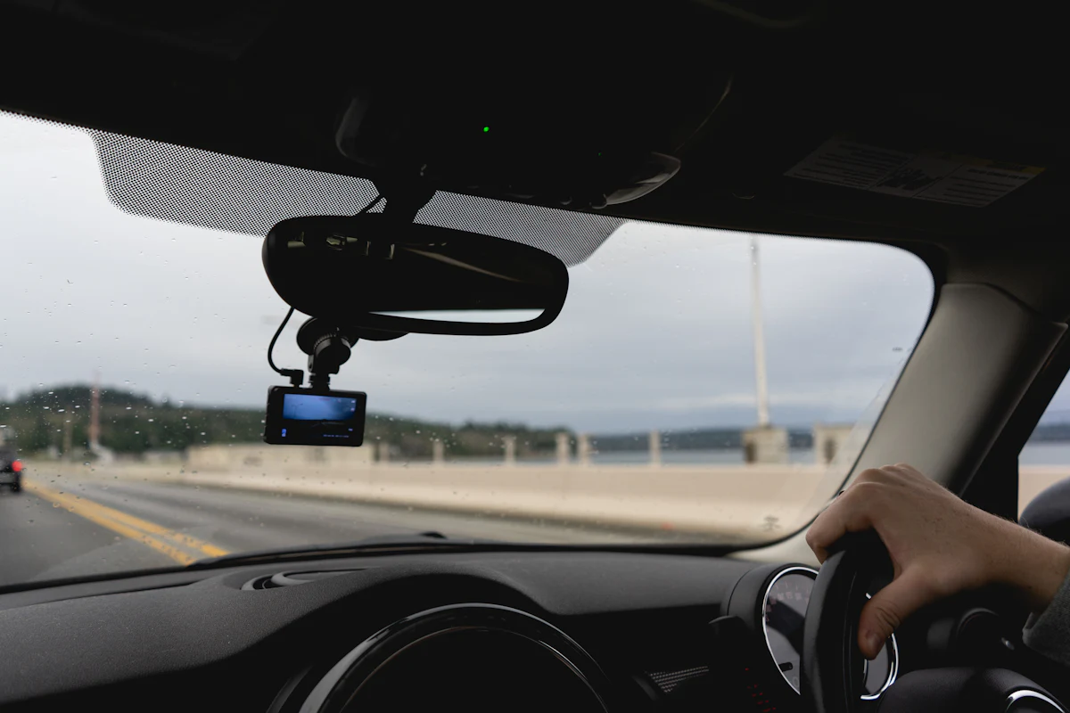 A dash cam mounted beside the rear-view mirror, seen from the driver’s seat on an open road.