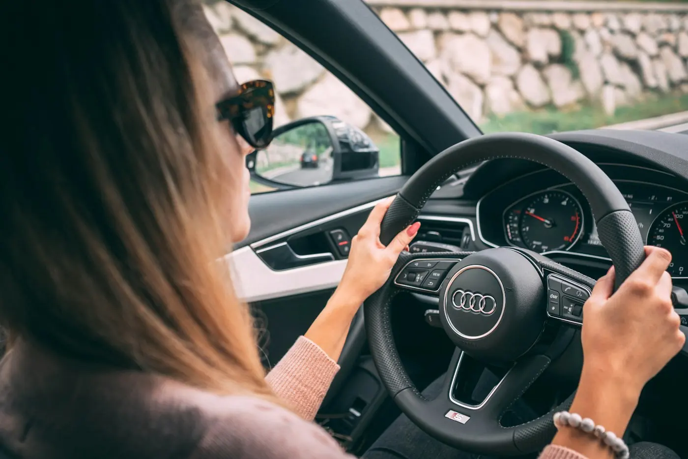 A woman in sunglasses driving, both hands on the wheel.