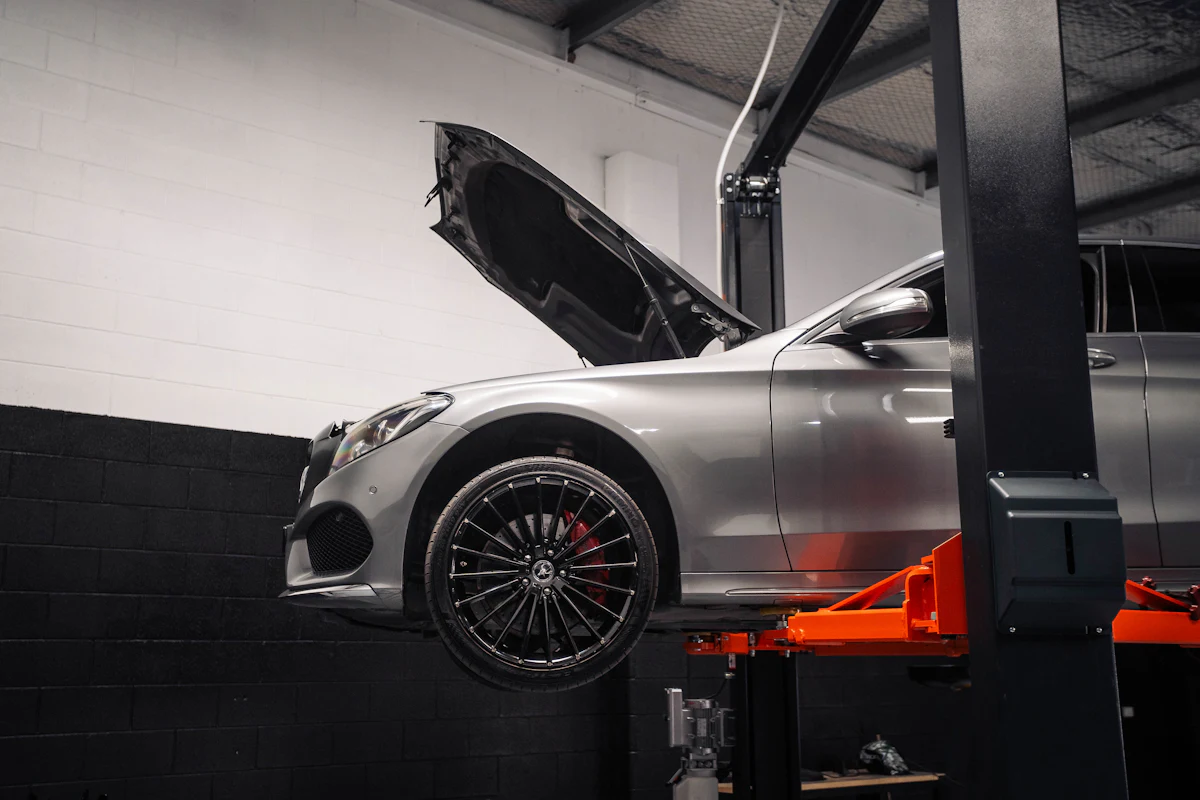 A silver car raised on a workshop hoist with its bonnet open.