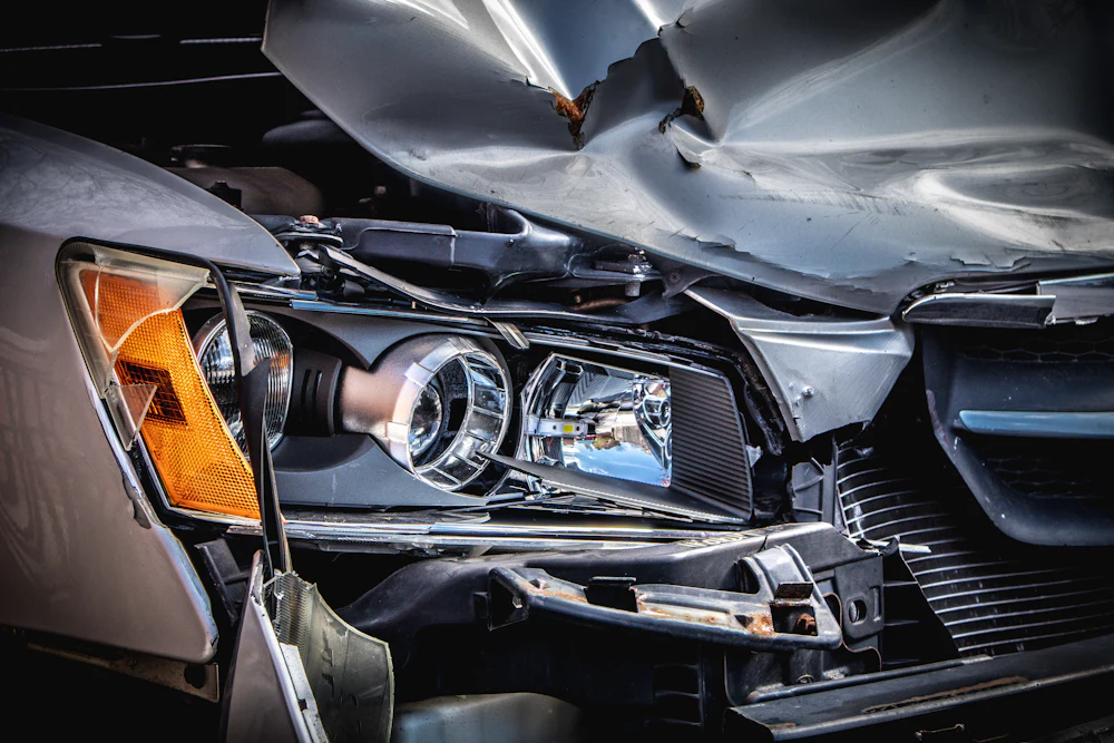 The front of a silver car crushed in a crash, bonnet folded and headlight broken.