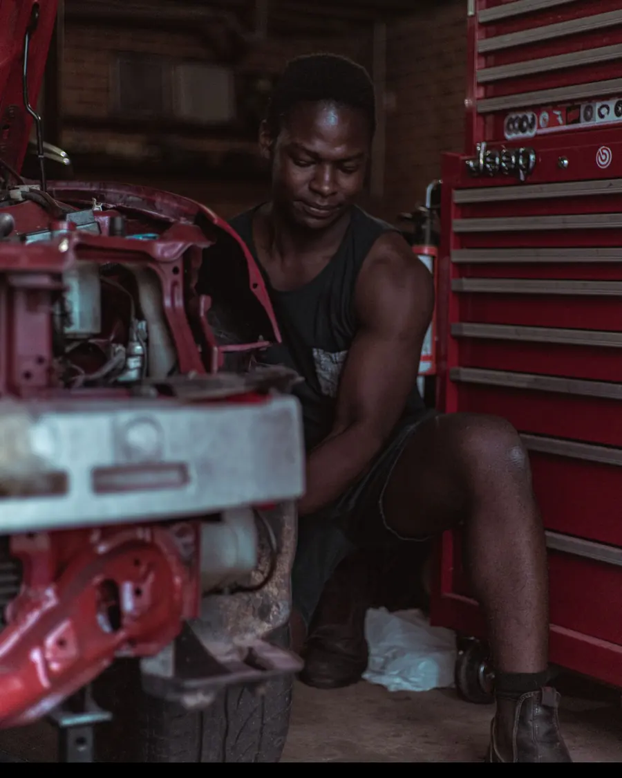 A panel beater kneeling beside a car with its front stripped back for repair.