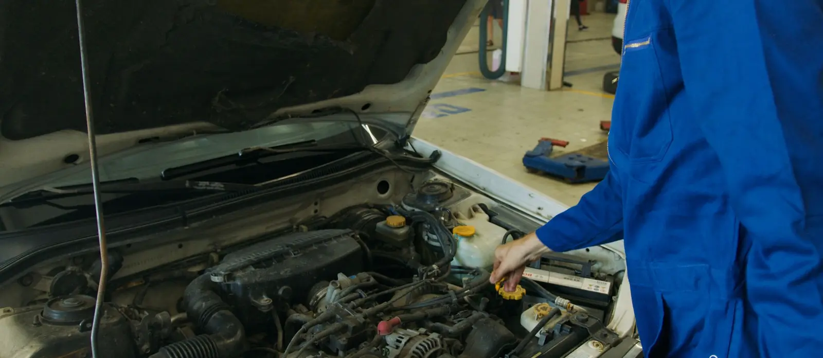 A mechanic working under the bonnet of a car in a repair workshop.