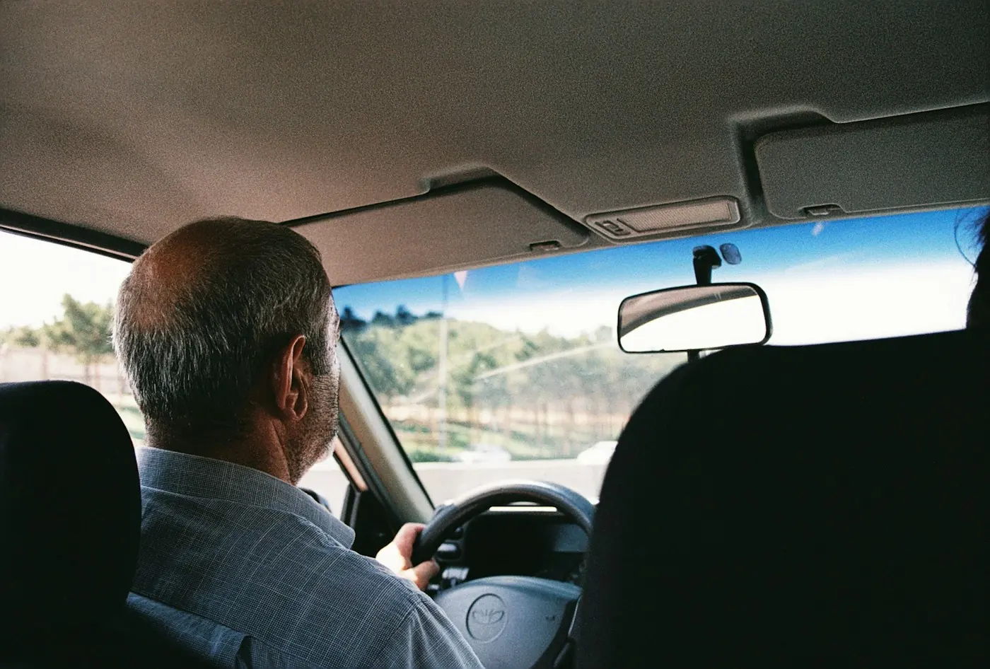 An older driver with both hands on the wheel, driving through the city.