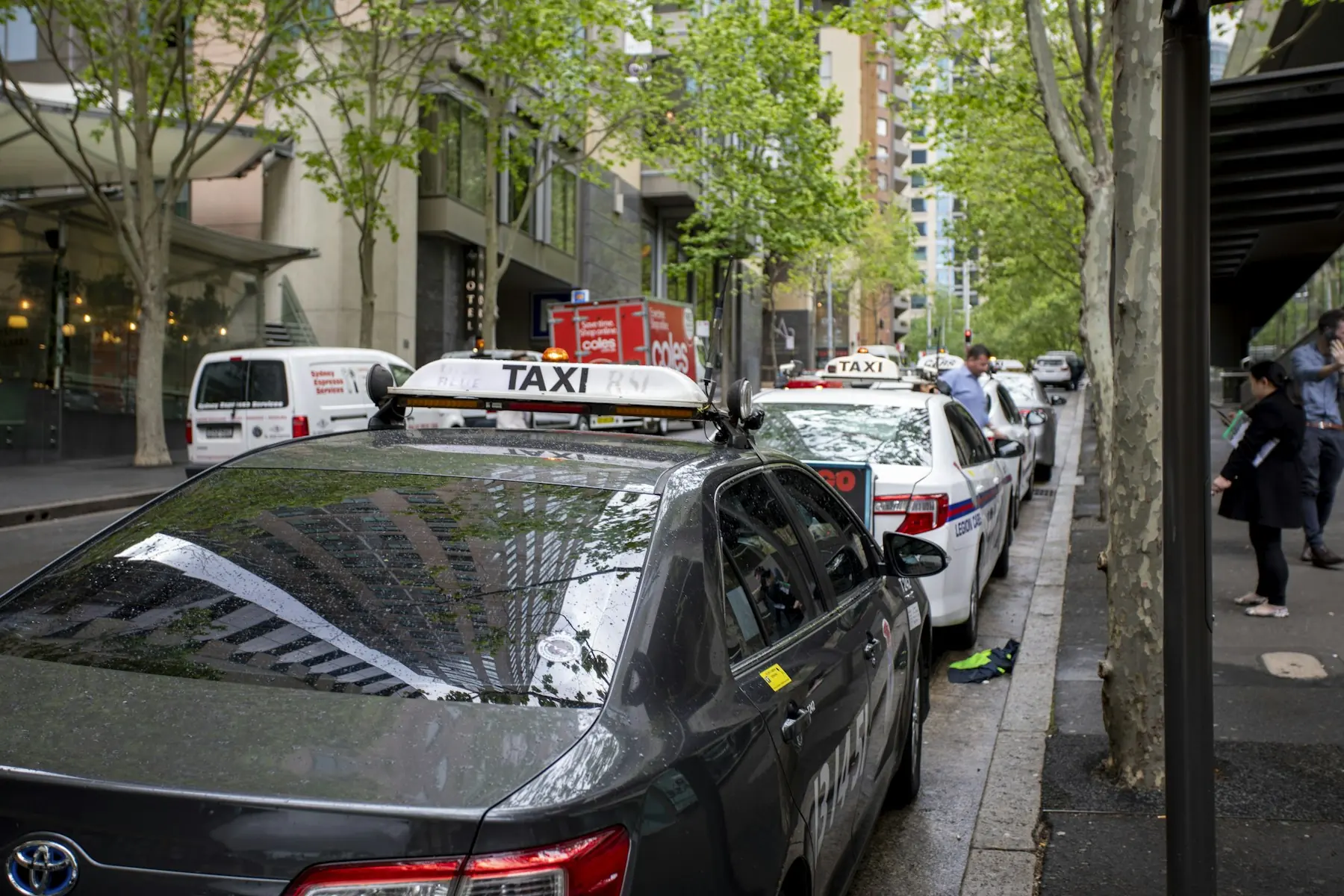 A line of taxis waiting at a rank on a city street.