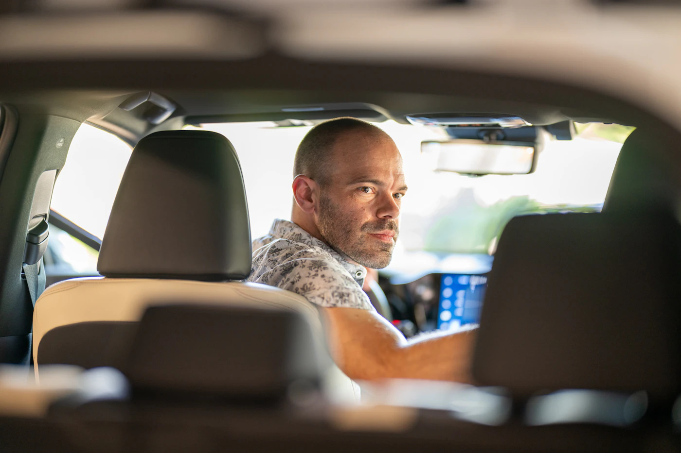 A driver turning around in his seat to talk to a passenger in the back of the car.