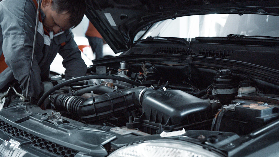 A mechanic leaning over an open car bonnet, checking the engine.